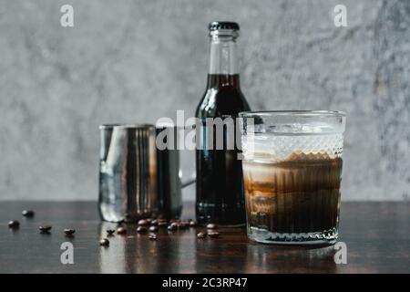 Kalter Kaffee mit Milch im Glas in der Nähe Flasche, Milchkännchen und Kaffeebohnen auf Holztisch Stockfoto