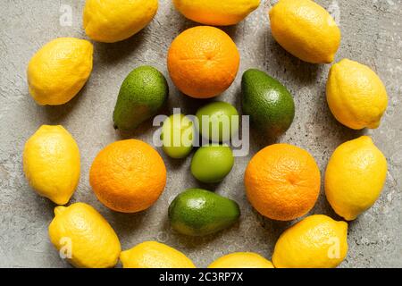 Draufsicht auf bunte Orangen, Avocado, Limetten und Zitronen im Kreis auf grauer Betonoberfläche angeordnet Stockfoto