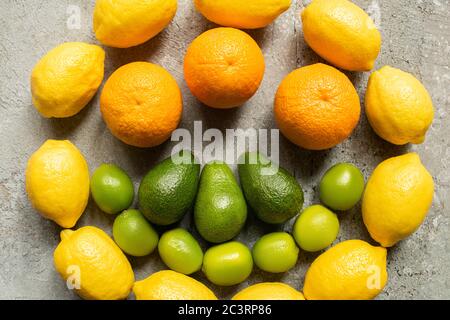 Draufsicht auf bunte Orangen, Avocado, Limetten und Zitronen im Kreis auf grauer Betonoberfläche angeordnet Stockfoto