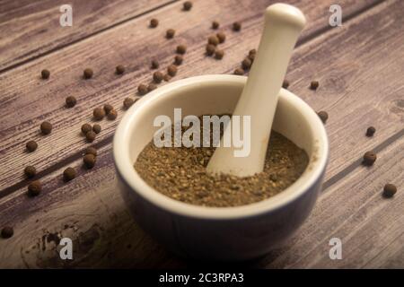 Piment in einem Keramikmörtel und verstreut Piment auf einem Holztisch. Nahaufnahme Stockfoto