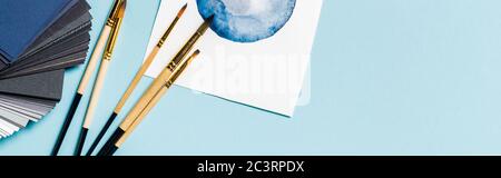 Panoramischer Ausschnitt der Pinsel neben der Aquarellzeichnung und Farbfelder auf der blauen Oberfläche Stockfoto
