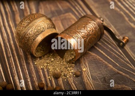 Eine offene manuelle Gewürzmühle und eine Streuung von gemahlenem Allspice auf einem Holztisch. Nahaufnahme Stockfoto