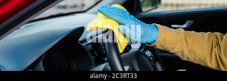 Beschnittene Ansicht des Menschen in Latexhandschuhen mit antiseptischem Spray und Lappen für die Autoinnendesinfektion während der Coronavirus-Pandemie, Panorama-Orientierung Stockfoto