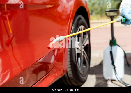 Beschnittene Ansicht des Spezialisten in Schutzanzug Reinigung Auto mit Desinfektionsmittel Spray während covid-19 Pandemie Stockfoto