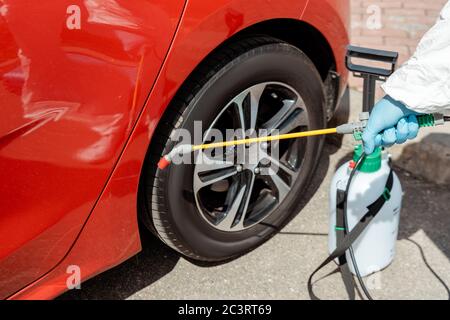 Beschnittene Ansicht des Spezialisten in Schutzanzug Reinigung Auto mit Desinfektionsmittel in Sprühbeutel während covid-19 Pandemie Stockfoto