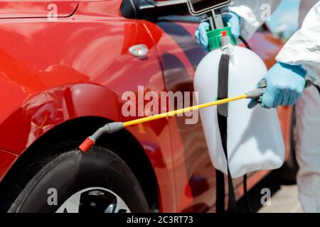 Beschnittene Ansicht des Arbeiters in Schutzanzug Reinigung Auto mit Desinfektionsmittel in Sprühbeutel während Coronavirus Pandemie Stockfoto