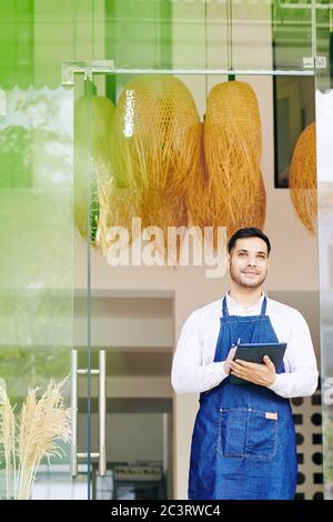 Ehrgeiziger, verträumter Cafe-Besitzer, der in Eingangstüren steht und seine Gedanken und Ideen zur Geschäftsentwicklung aufschreibt Stockfoto