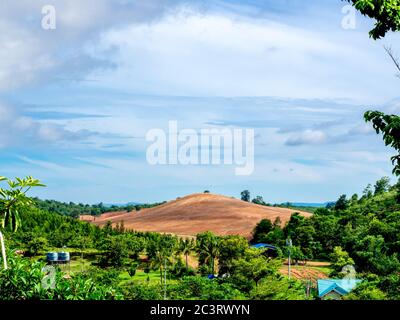 Schöne kahle Berg stehen umgeben mit Landschaft mit vielen frischen grünen Baum und blauen Himmel auf dem Land. Stockfoto