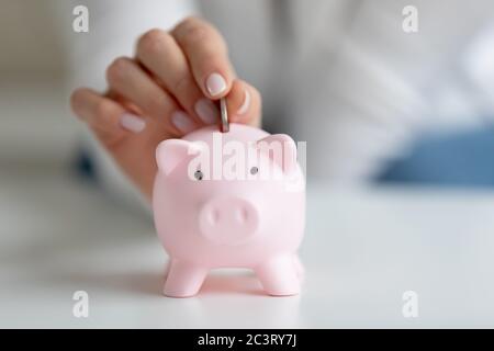 Nahaufnahme Bild weibliche Finger legt Münze in der Sparschwein Stockfoto