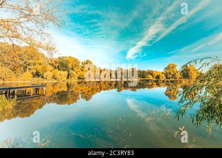 Bunte Laubbäume spiegeln sich an einem schönen Herbsttag in einem ruhigen Teichwasser. Helle Herbstbäume mit ruhigem Himmel, Herbstlaub über dem See Stockfoto