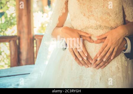 Vier Hände auf dem Bauch der schwangeren Frau. Paar posiert ein Herz mit ihren Fingern auf dem Bauch der werdende Mutter Stockfoto