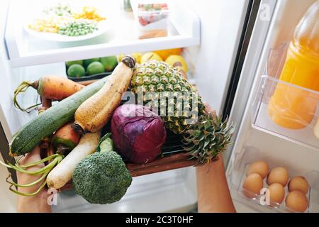 Hände der Person, die Tablett mit frischem Gemüse und Obst aus dem Kühlschrank Stockfoto