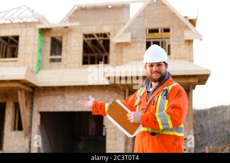 Europäischer Architekt in orange Arbeitskleidung hält Notebook auf der Baustelle. Stockfoto