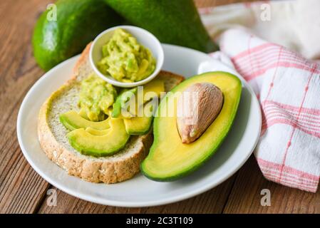 Avocado in Scheiben geschnitten Hälfte und Avocado Dip püriert auf weißem Teller Hintergrund Früchte gesunde Ernährung Konzept / Avocado Toast Stockfoto