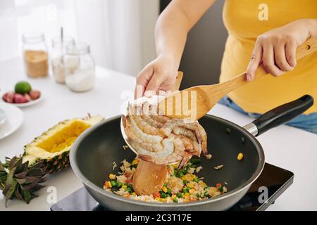 Beschnittenes Bild der Hausfrau, die in der Pfanne gebratenen Reis Garnelen zugab Stockfoto