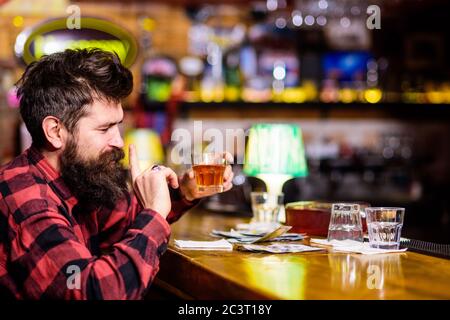Betrunkenes und entspanntes Konzept. Mann mit betrunkenem Gesicht sitzt allein in der Bar oder Pub in der Nähe der Theke. Hipster hält Glas mit Whiskey oder alkoholischem Getränk. Kerl verbringen Freizeit in der Bar, defokussed Hintergrund. Stockfoto