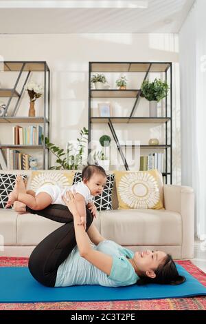 Glückliche junge Mutter mit kleiner Tochter, die während des Lockdown zu Hause auf einer Yogamatte arbeitet Stockfoto