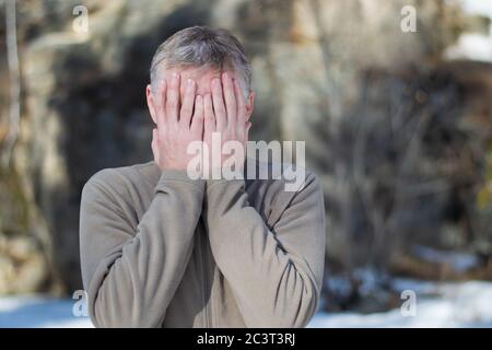 Porträt eines Mannes mittleren Alters auf der Straße, das Gesicht mit den Händen bedeckt. Ausdruck von Traurigkeit, Zweifel, Verzweiflung. Krisenkonzept. Stockfoto