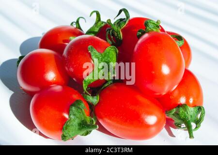 Frische kleine Kirschtomaten mit grünem Stiel auf hellem Hintergrund. Nahaufnahme. Selektiver Fokus Stockfoto