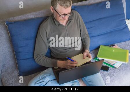 Ein Mitarbeiter des Unternehmens arbeitet von zu Hause aus in bequemer Kleidung, sitzt auf einem Sofa. Arbeiten Sie von zu Hause aus online, Remote-Arbeit während des Coronavirus. Stockfoto