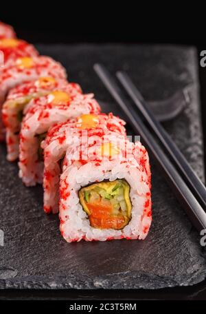 Uramaki Sushi-Rollen mit rotem Kaviar mit Lachs und Gurke gefüllt bedeckt. Serviert auf einem schwarzen Steinbrett. Stockfoto