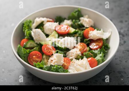 Salat mit Grünkohl, Tomaten, Gurken und Mozzarella in weißer Schüssel Stockfoto