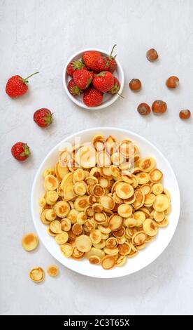 Pfannkuchen Müsli in einer Schüssel mit frischen Erdbeeren und Nüssen auf hellem Hintergrund. Leckeres und trendiges Frühstück. Bio-Holländische Mini-Pfannkuchen. Stockfoto