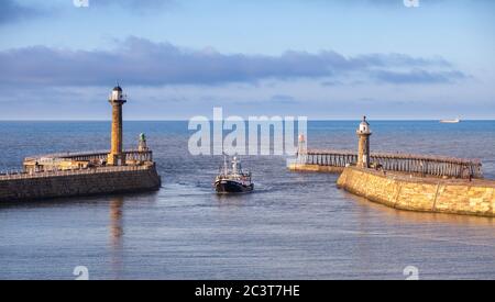 Ein Fischerboot, das in den Hafen von Whitby zwischen den West- und Ostpiers einfährt Stockfoto