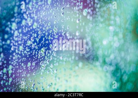 Regen fällt auf Fenster mit abstrakten lila grünen Baum im Hintergrund. Stockfoto