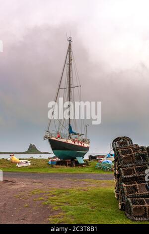 Eine Yacht, die für die Wartung gezogen wurde, mit dem Schloss und dem Hafen dahinter, von The Common, Lindisfarne, Holy Island, Northumberland, England, Großbritannien Stockfoto