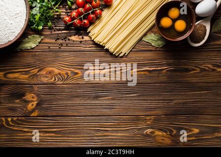 Pasta Hintergrund. Verschiedene Arten von trockenen Nudeln mit Gemüse und Kräutern auf einem Holztisch. Stockfoto