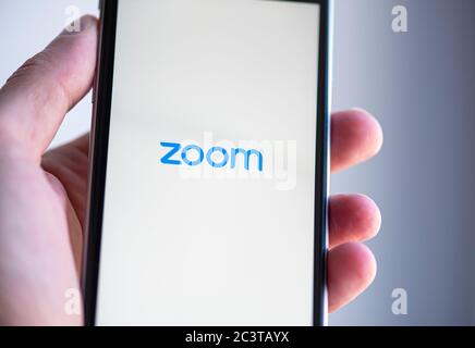 BERLIN - JUN 22: Mann mit Handy mit Logo der ZOOM-Anwendung am 22. Juni in Berlin am Bildschirm. 2020 in Deutschland Stockfoto