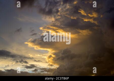 Farbenfrohe orange Sonnenuntergänge mit grauen Sturmwolken, die sich vor einer Wetterfront versammeln, in dramatischer Formation, die von der glühenden Sonne beleuchtet wird Stockfoto