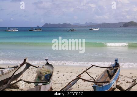 Kleine Jukungboote und brechende Welle in Lombok. Kuta Lombok ist ein exotisches Paradies auf der indonesischen Insel, mit wunderschönen weißen Sandstränden und Buchten Stockfoto