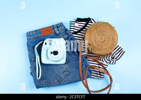 Blaue Jeans Shorts, gestreiftes Hemd, Rattan Tasche auf blauem Hintergrund. Flach liegend, Draufsicht. Sommerliches Outfit-Konzept Stockfoto