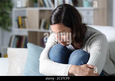 Nachdenkliche traurige Erwachsene Frau, die auf dem Sofa im Wohnzimmer zu Hause sitzt Stockfoto