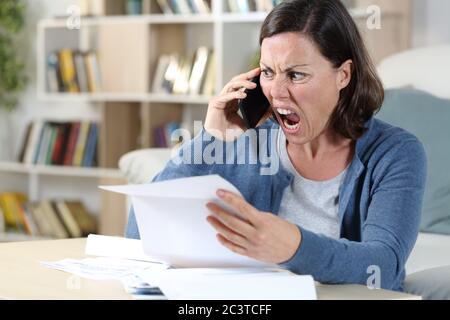 Wütend Erwachsene Frau ruft auf Smartphone mit Brief sitzen im Wohnzimmer zu Hause Stockfoto