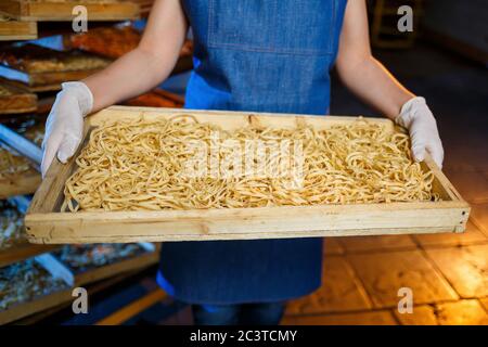 Arbeiter mit einer Schachtel Nudeln. Das Mädchen arbeitet an der Herstellung von Spaghetti. Nudeln machen. Pasta-Fabrik. Stockfoto