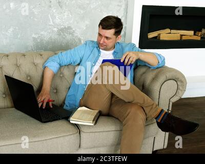 Remote-Arbeit. Ein junger Mann arbeitet zu Hause mit einem Laptop und Dokumenten. Stockfoto