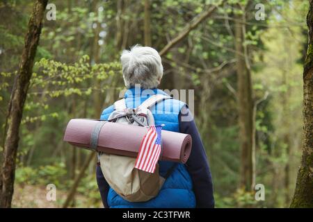 Rückansicht auf aktiven Senior Mann trägt Rucksack mit amerikanischer Flagge, während Wandern im Wald, Copy Space genießen Stockfoto