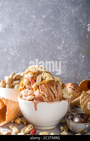Erdnussbutter-Eis. Süßes Erdnusseis mit Erdnussbutter-Belag und vielen Erdnüssen, auf grauem Steinhintergrund mit Eiscreme-Waffelkegel Stockfoto