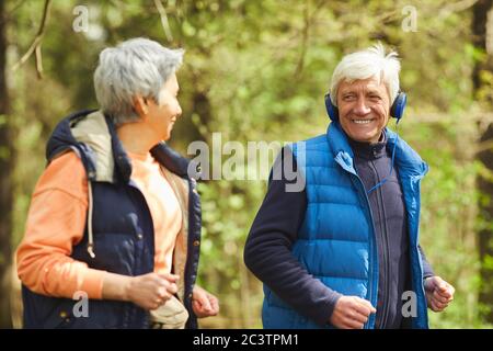 Waist up Porträt von aktiven Senioren Paar laufen im Wald von Sonnenlicht beleuchtet und einander glücklich zu schauen Stockfoto