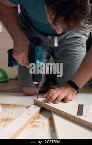 Mann, der zu Hause Renovierungsarbeiten macht, Bohren mit einem Schraubendreher. Gruppe von Reparaturwerkzeugen auf weißem Hintergrund.