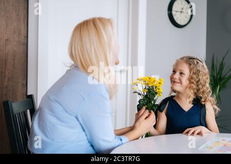 Liebevolle Tochter gibt Blumenstrauß Blumen zu ihrer Mutter. Mädchen gibt ein Geschenk an ihre geliebte Mutter. Stockfoto