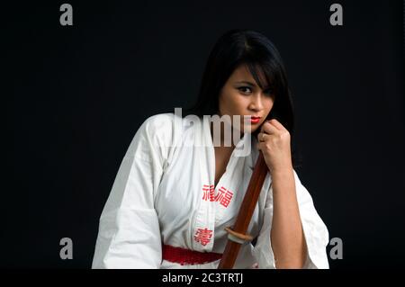 Junge asiatische Frau mit einem Bokken (ein japanisches Holzschwert, das zum Üben verwendet wird) auf schwarzem Hintergrund Stockfoto