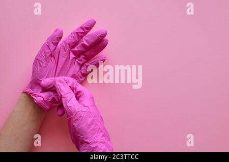 Hände in rosa Handschuhen auf rosa Hintergrund. Coronavirus covid-19-Virenpräventionskonzept. Rosa Hintergrund, Copyspase. Layout, Draufsicht, flach liegend. Stockfoto