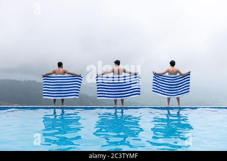 Drei junge asiatische Mann stehen am Infinity Pool mit entsprechenden Handtücher an einem nebligen Tag in den Bergen. Stockfoto