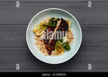 Eine köstliche Schüssel mit Jerk Huhn, Reis und Gemüse, in einer hellblauen Schüssel auf einem verzweifelten dunklen Holzhintergrund erschossen Stockfoto