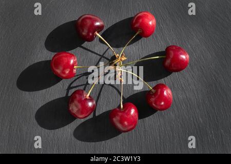 Kirschen flach Design Hintergrund. Kirsche mit Stielen auf schwarzem Teller Hintergrund, Draufsicht Stockfoto