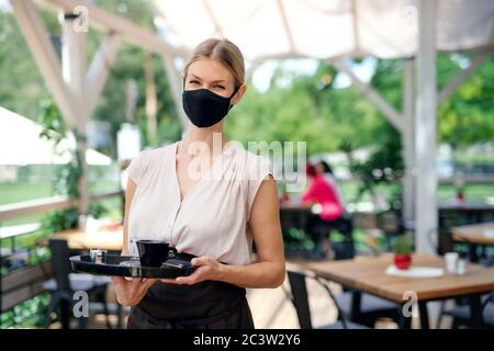 Kellnerin mit Gesichtsmaske serviert Kunden im Freien auf Terrasse Restaurant. Stockfoto